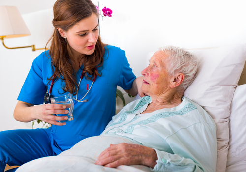 caregiver bringing water to elderly woman