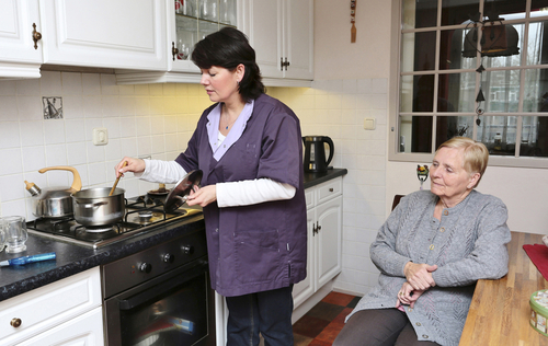 A caregiver is making soup for an elderly woman