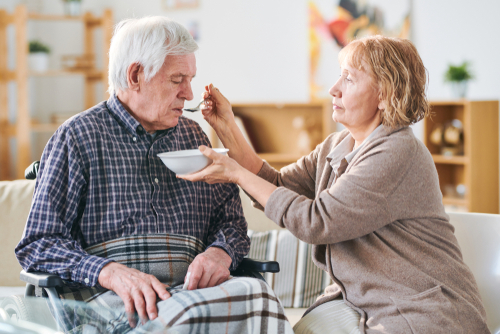 Aged woman holding bowl with soup for husband